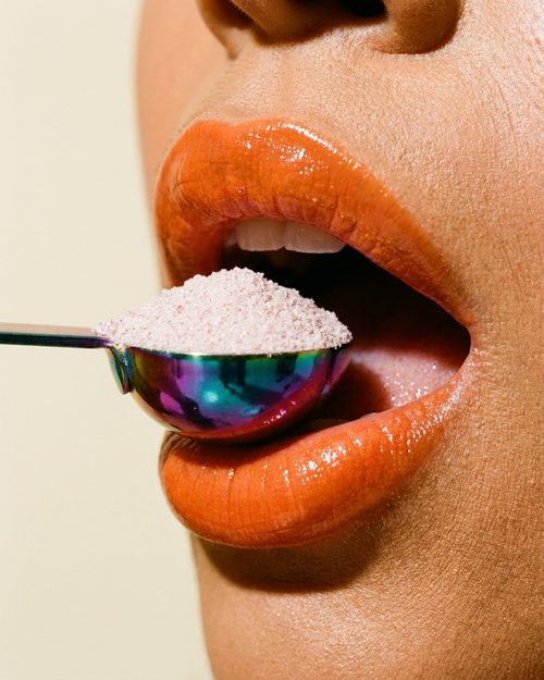 Close-up of glossy orange lips and a spoon of electrolyte powder