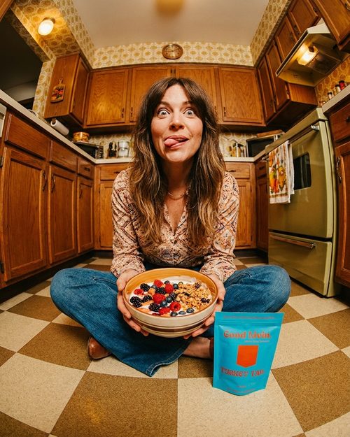 Fisheye shot of a woman on a checkerboard kitchen floor with a cereal bowl