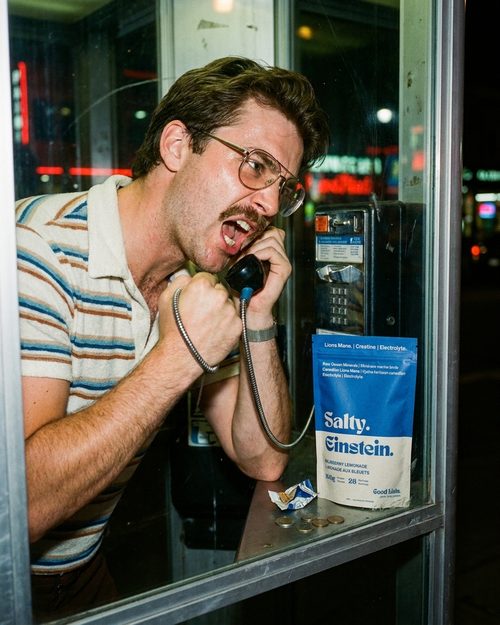 Man yelling into a payphone with a Salty Einstein pouch on the ledge
