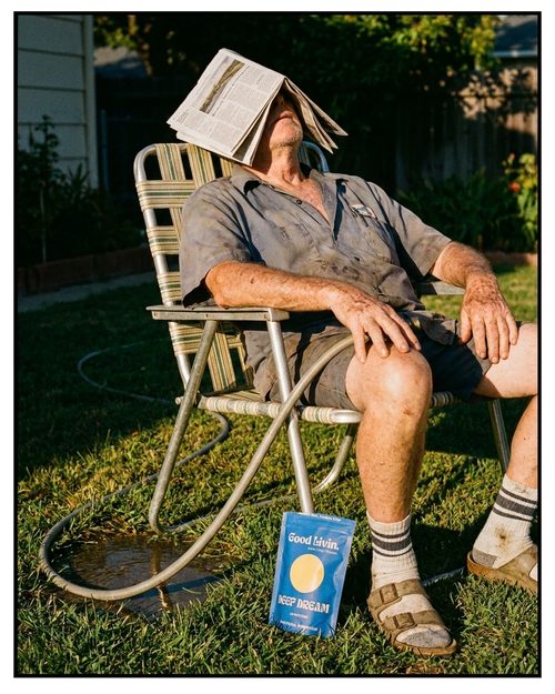 Man asleep on a lawn chair with a newspaper over his face and a Deep Dream pouch